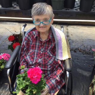 A person in a wheelchair holding a vibrant pink flower in an outdoor garden setting.