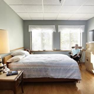 A hospital room with a bed, chair, and large windows letting in natural light.