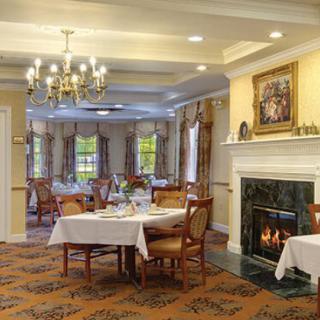 A cozy and elegant dining room with a chandelier and fireplace, featuring neatly set tables.