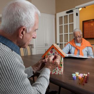 Two seniors engaging in a birdhouse painting activity at a table indoors.