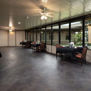 A spacious dining area with tables and chairs, featuring large windows and a ceiling fan.