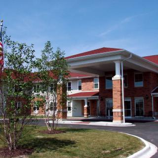 A two-story brick building with a red roof and entrance, surrounded by trees and an American flag.