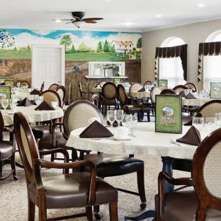A beautifully decorated dining room with neatly arranged tables and chairs, featuring a scenic mural on the wall.