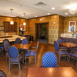 A cozy dining area with wooden furniture and blue upholstered chairs, featuring decorative wallpaper and a chandelier.