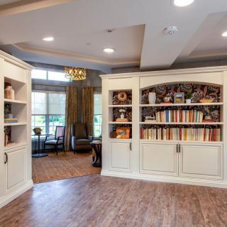 A cozy library room with built-in bookshelves and wood flooring, featuring a comfortable seating area by the window.