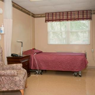 A tidy hospital room with a single bed, armchair, and a window with checkered curtains.