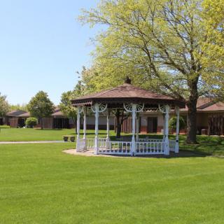 A charming gazebo sits in the middle of a lush green park surrounded by trees under a clear sky.