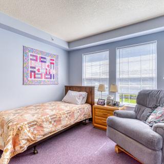 A cozy bedroom featuring a single bed, armchair, and large windows letting in natural light.