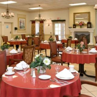 An elegant dining room with tables set for a meal, featuring red tablecloths and floral centerpieces.