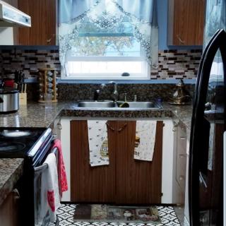 A modern kitchen with wooden cabinets, a stone countertop, and patterned curtains above the window.