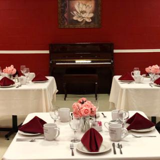 An elegantly arranged dining room featuring tables set for a special occasion, accented by floral arrangements and a classic piano.