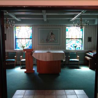 An interior view of a small chapel with an altar and stained glass windows.