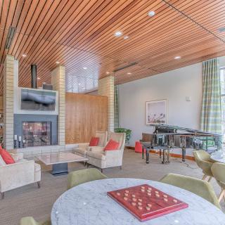 A modern living room with a wooden ceiling, comfortable seating around a fireplace, and a chessboard on the table.