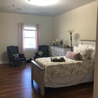 A cozy bedroom with a bed, dresser, and two chairs by the window.