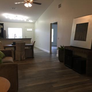 A modern open-concept living and dining area with a view of the kitchen, featuring wood flooring and a ceiling fan.