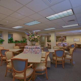 A well-lit, carpeted dining area with multiple tables and chairs, decorated with flowers.