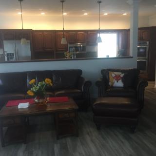 An open-concept living room with a view of the kitchen, featuring comfortable seating and warm decor.