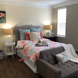 A cozy bedroom with a floral bedspread, decorative pillows, and warm lighting from bedside lamps.