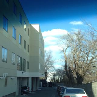 A view of a parking area next to a building, showcasing surrounding trees and a clear sky.
