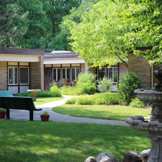 A tranquil garden area with a pathway, surrounded by lush greenery and buildings.