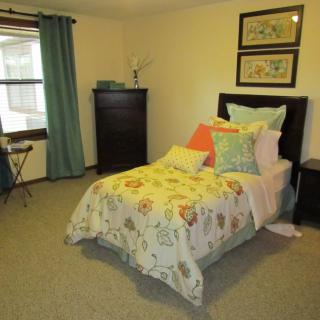 A cozy bedroom with a neatly made bed featuring colorful pillows and a floral-patterned comforter.