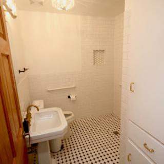 A clean and minimalist bathroom featuring white tiles and a classic black and white floor pattern.