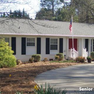 A suburban one-story house with a red door and an American flag in the front yard.