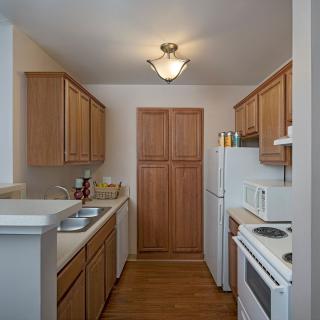 A modern apartment kitchen with wooden cabinets, a stove, refrigerator, and microwave.
