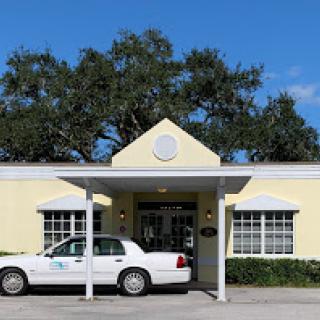 A white taxi parked in front of a yellow building with a welcoming entrance.