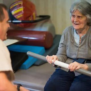 An elderly woman participating in a physical therapy session, engaging in exercises with support.
