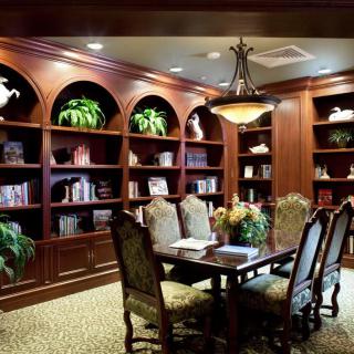 A cozy library with wooden bookshelves and a dining table surrounded by chairs, accented with plants and warm lighting.