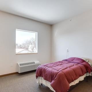 A minimalist bedroom with a single bed and purple bedding, featuring a bright window.