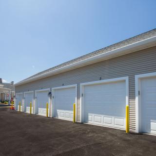 A row of storage garages with closed white doors under a clear blue sky.