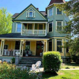 A charming Victorian house with a spacious porch and lush garden on a sunny day.