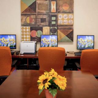 A well-organized office space featuring computers, a printer, and decorative art, complemented by a vase of sunflowers on the table.
