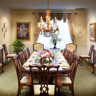 A beautifully furnished dining room with a long table set for a formal dinner, decorated with a floral centerpiece and illuminated by an elegant chandelier.