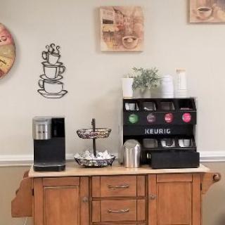 A neatly organized coffee station with a machine, cups, and decor on a wooden cabinet.
