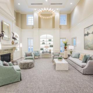A spacious and elegantly decorated living room featuring modern furniture, a chandelier, large windows, and a fireplace.