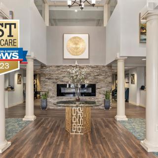 A modern and elegant lobby featuring a fireplace, wooden flooring, and decorative columns. An award emblem is displayed in the upper left corner.