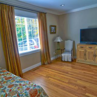 A cozy bedroom with a TV, window with curtains, and wooden flooring.