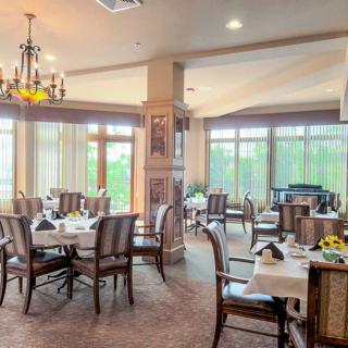 An elegant dining room with beautifully set tables, soft lighting, and large windows overlooking greenery.