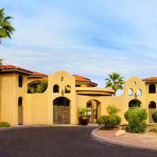 A large Mediterranean-style luxury home with a warm yellow facade and surrounded by palm trees.