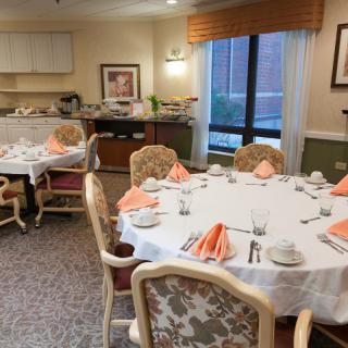 A neatly arranged dining room with tables set for a meal, featuring elegant chairs and orange napkins.