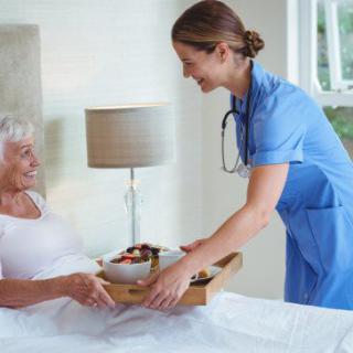 A nurse delivering a meal to an elderly patient in a hospital room.