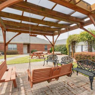 A peaceful courtyard with a wooden pergola and swing, surrounded by benches and greenery.