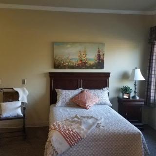 A cozy bedroom with a neatly made bed, a lamp on the nightstand, and artwork above the headboard.