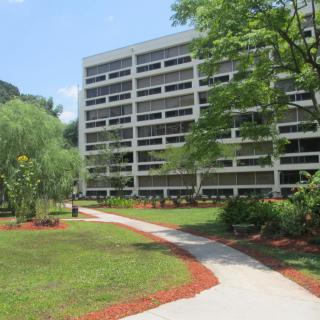 A modern multi-story building surrounded by greenery and a landscaped path.