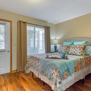 A cozy bedroom with a decorative bedspread, hardwood flooring, and natural light streaming through the window.