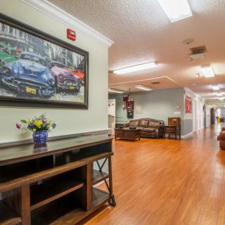 A well-lit hallway featuring wooden floors, artwork on the walls, and neatly arranged furniture.