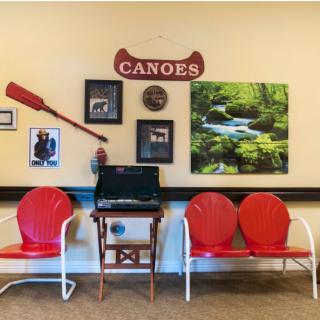 A waiting area with red chairs and a canoe-themed wall, featuring decorative paddles, photo frames, a nature painting, and a computer station.